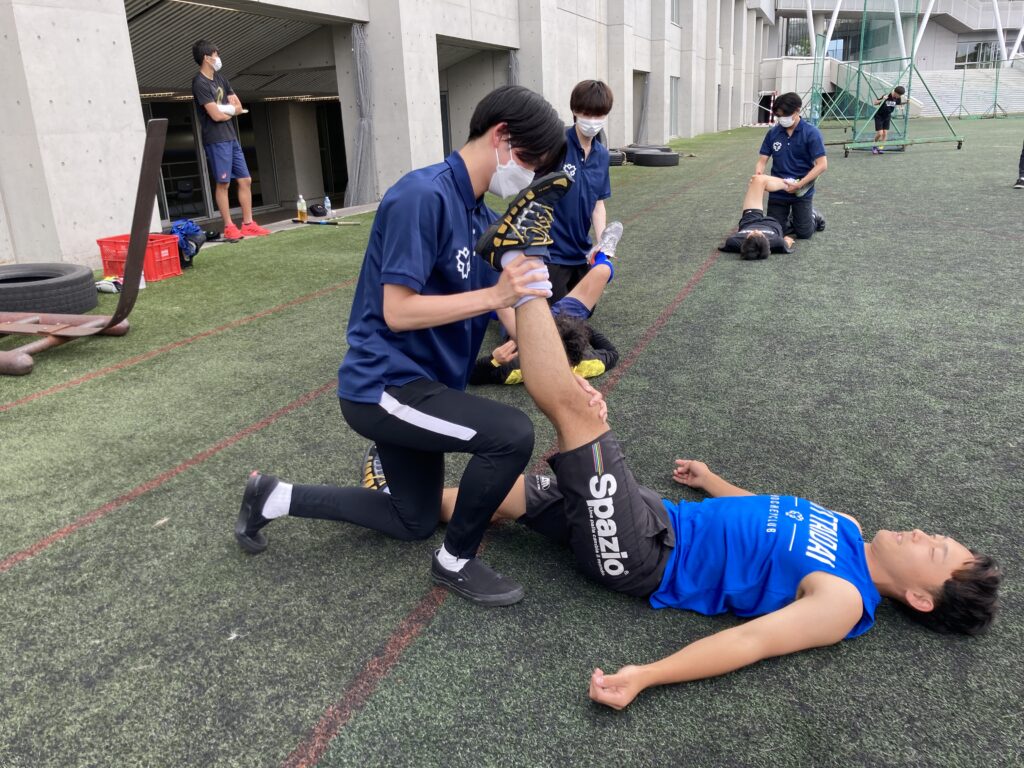 練習前のストレッチをサポートする学生