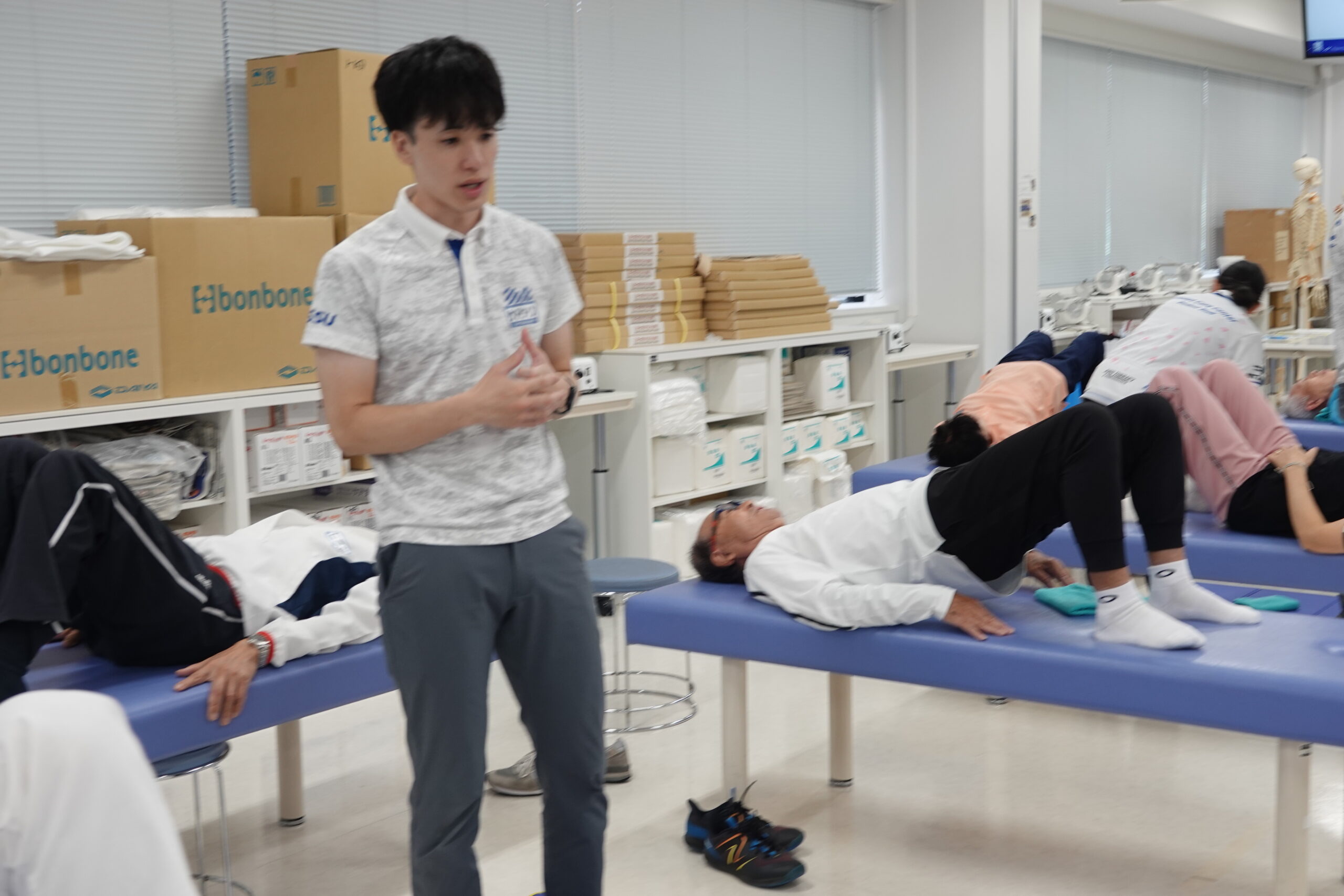 祁答院隼人先生が運営スタッフとして参加し，参加者がベッド上で体操に取り組む様子