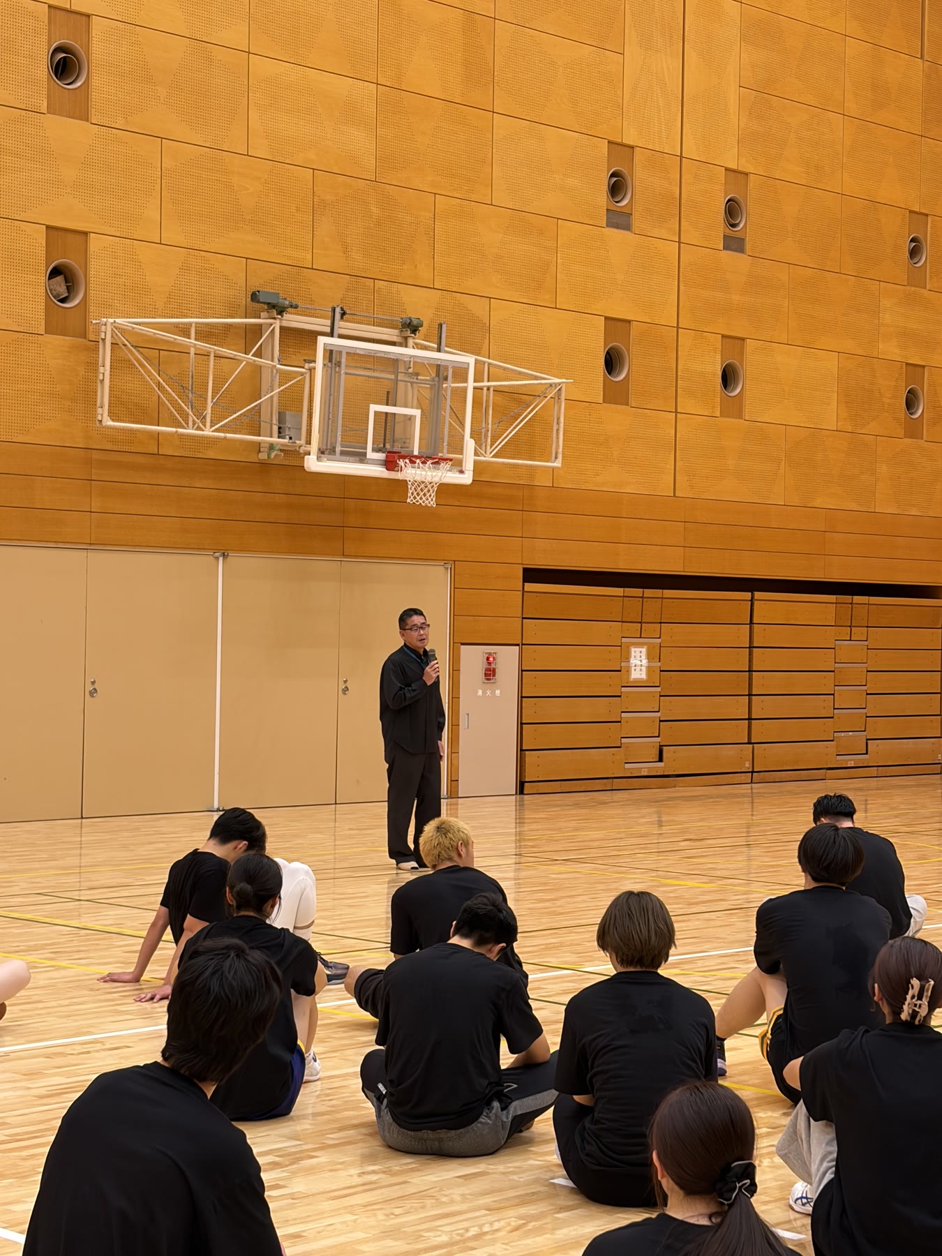 体育館で大会の締めくくりの話を聞く学生たち
